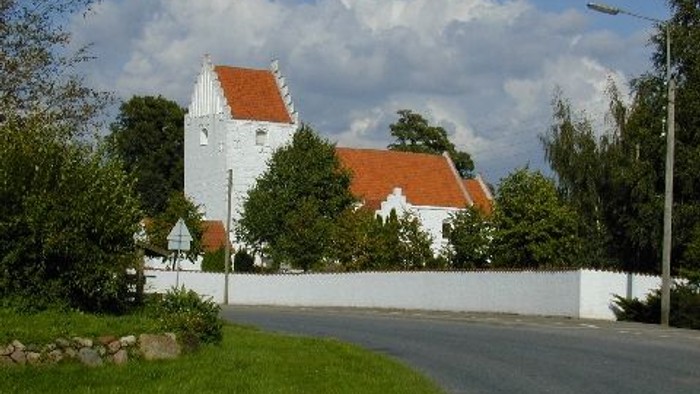 En hyggelig hvid kirke med røde tage gemt bag et hvidt hegn på en solskinsdag.