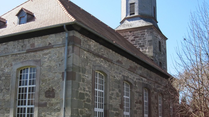 Außenansicht der evangelischen Kirche in Oberelsungen. Das Gebäude besteht aus hellem Naturstein mit hohen Fenstern.