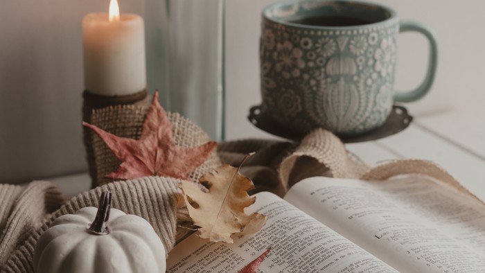 Gemütliche Herbstszene mit Kürbissen, Kerze, Buch, Tasse und Jutestoff.