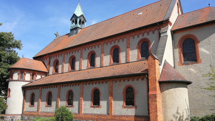 Das Bild zeigt eine rote Backsteinkirche mit weißem Putz und grünem Turm.