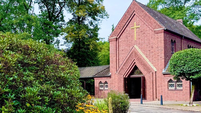 Idyllische Backsteinkirche, eingebettet in einen farbenfrohen Garten und üppiges Grün mit einem beschaulichen Weg.