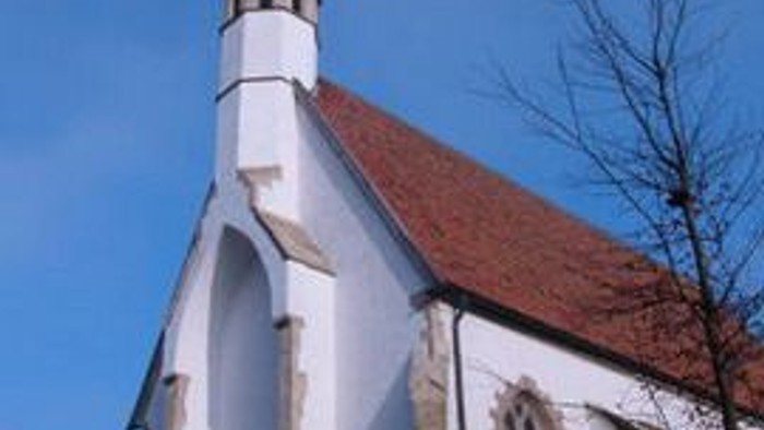 Eine malerische weiße Kirche mit einem steilen roten Ziegeldach und einem hohen Turm vor klarem Himmel.