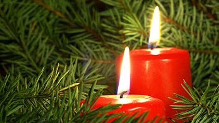 Zwei rote Kerzen, umgeben von Tannengrün, die eine festliche Weihnachtsstimmung hervorrufen.