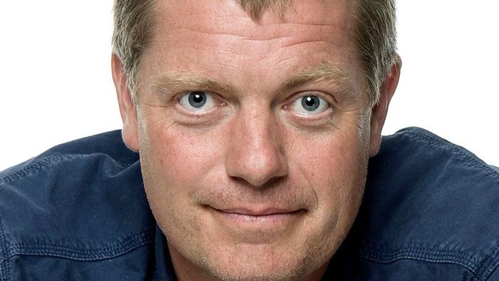 En mand med kort, grånende hår iført en blå skjorte poser med et neutralt udtryk.