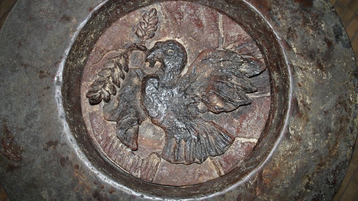 En rustet metalplade med en udgraven relief af en fugl.