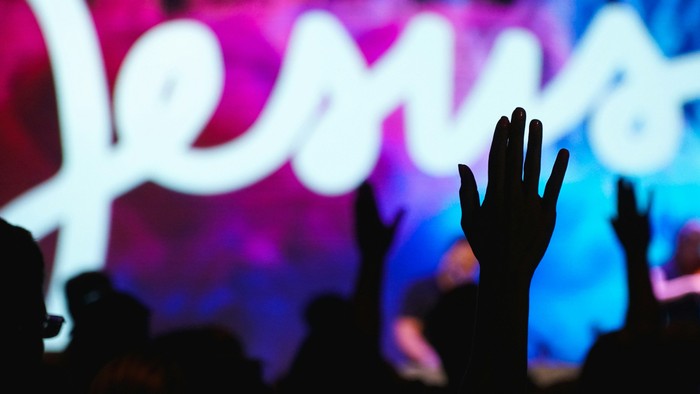 Menge mit erhobenen Händen bei einem lebhaften Konzert mit der beleuchteten Aufschrift „Pentatonix“ auf der Bühne.