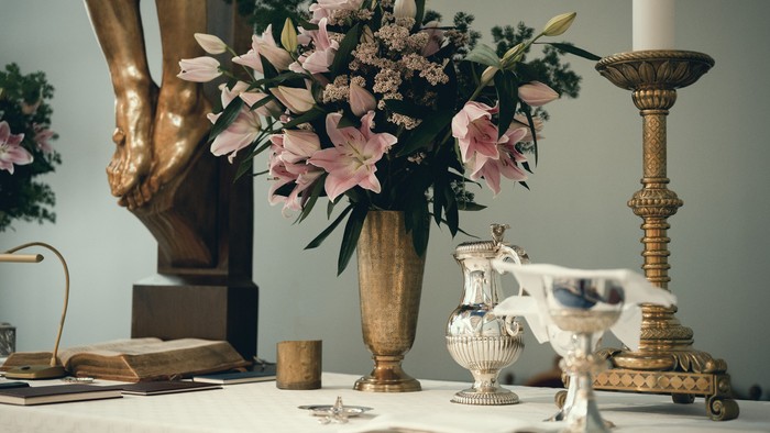 Elegant vintage-borddækning med prydvaske med liljer, antikke bøger og dekorative messingstager.