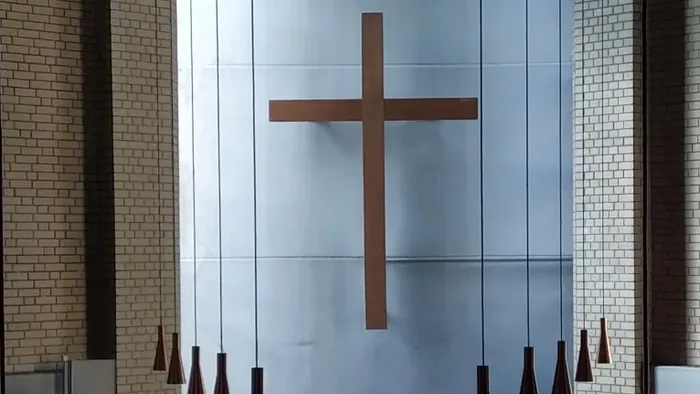 Ein Kircheninneres mit einem großen Holzkreuz an der Wand und mehreren Hängelampen.