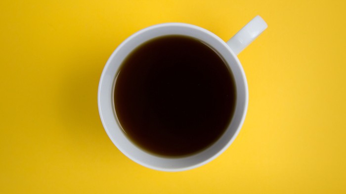 Eine weiße Tasse mit schwarzem Kaffee auf gelbem Hintergrund