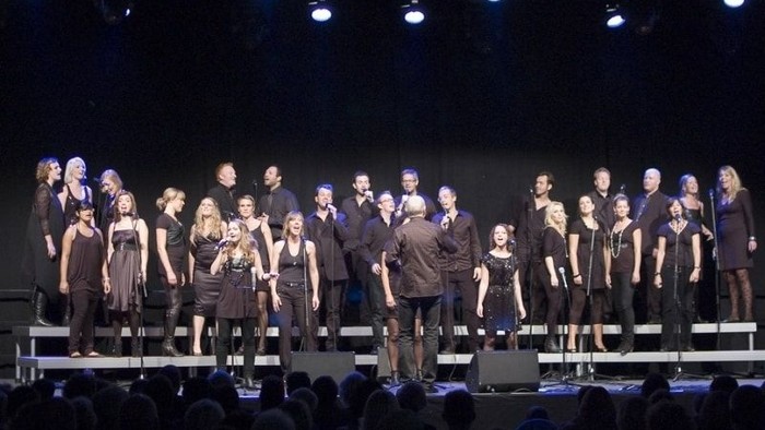 En stor gruppe på scenen med lys og publikum foran
