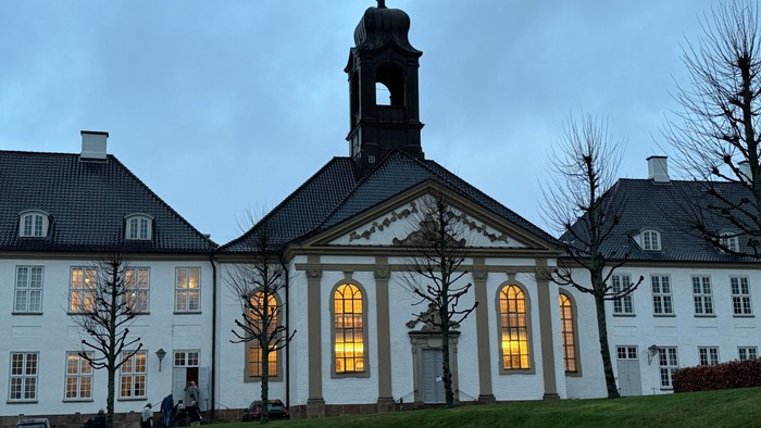 Stor hvid bygning med klokketårn og lysende vinduer.