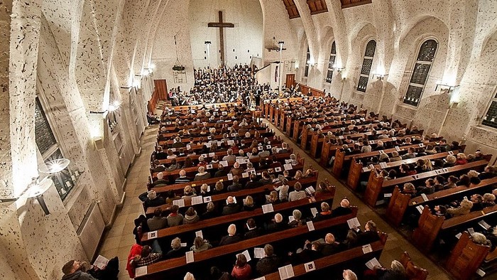 Große Kirche mit vielen Gläubigen in Reihen sitzend, ein Kreuz und ein Altar sind sichtbar