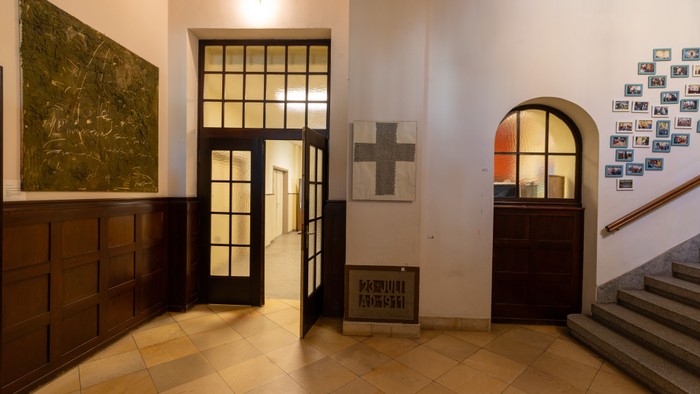 Ein eleganter Flur mit Holzschränken, gerahmten Kunstwerken, einem Kreuz und einer Treppe mit gerahmten Fotos an der Wand.
