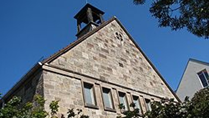 Steingebäude mit Uhrturm und Fenstern, teilweise von Bäumen verdeckt.