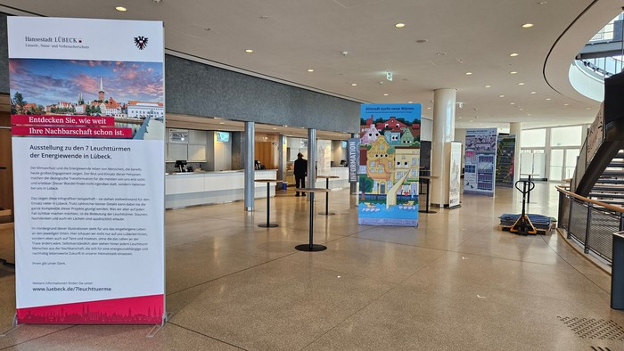 Moderner Empfangsbereich mit Informationsdisplays, bunten Plakaten und Abstandsmarkierungen in einem Unternehmens- oder öffentlichen Gebäude.
