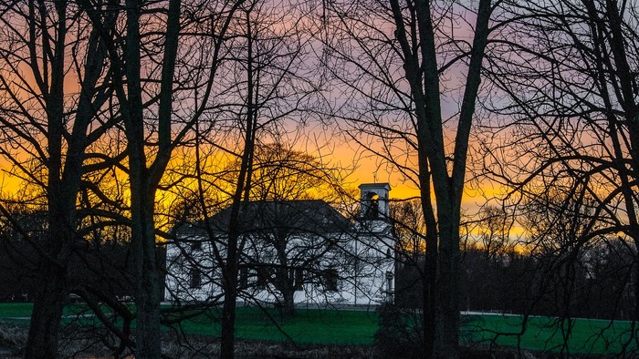 En præget gård med en stor skur og træer foran en rødgul solnedgang