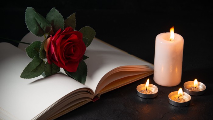an open Bible with a red rose placed on top of it and 4 lit candles