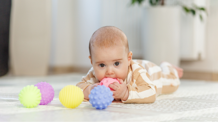 Nysgerrig baby på mavelegetid, der rækker efter farverige teksturerede bolde.
