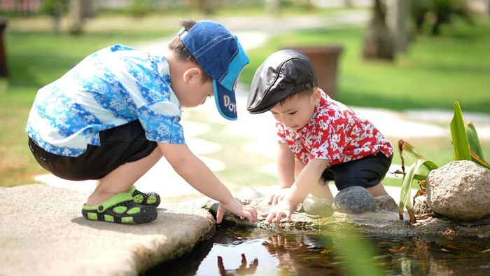 Zwei Kinder erkunden ein flaches Wasserbecken im Freien und untersuchen genau Steine und Wasser.