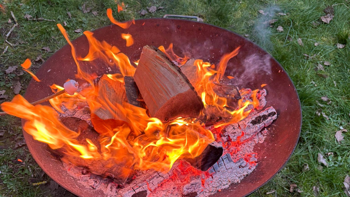 Ein tragbarer Grill mit glühender Kohle und Holzscheiten auf einer grasbewachsenen Fläche im Freien.