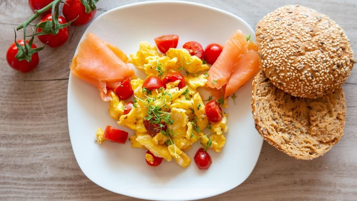 Ein herzhaftes Frühstück mit Rührei mit Tomaten, Karotten und einem Sesambrötchen.