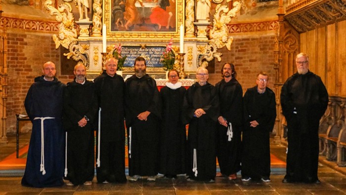Munke i traditionelle kjortler poser sammen inde i en prægtig kirke med religiøs kunst i baggrunden.