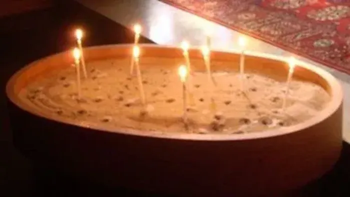 Eine Schale mit Sand hält fünf brennende Kerzen in einer gemütlichen, schwach beleuchteten Umgebung.