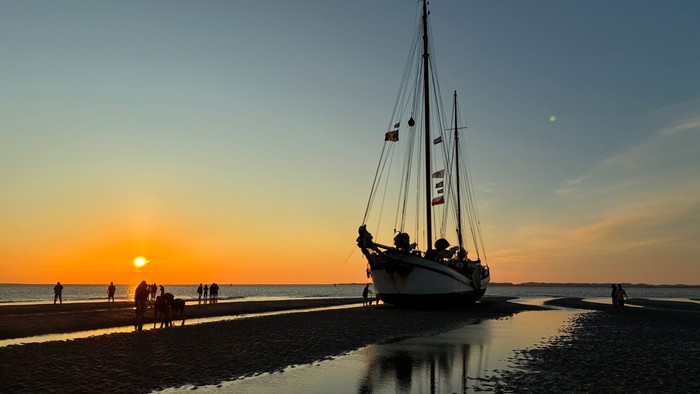 Segelboot am Ufer während des Sonnenuntergangs mit Menschen drumherum.