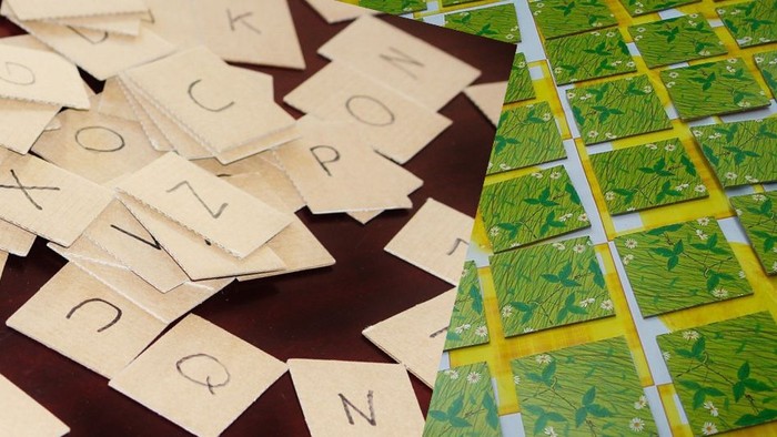 Scrabble-Steine und Spielsteine auf einer Holzoberfläche mit Buchstaben und grün gemusterten Karten angeordnet.