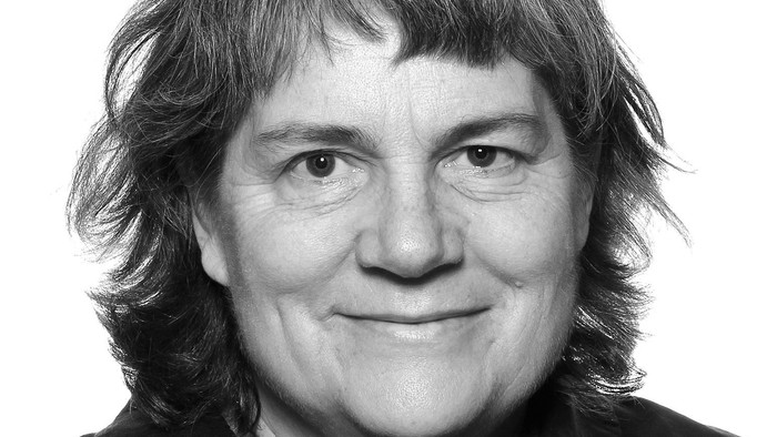 Et smilende portræt af en person med kort, bølget hår i en sort top.