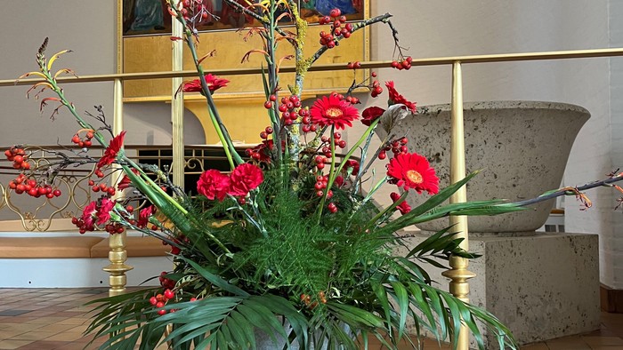 En blomstervase med røde blomster på en bænk.