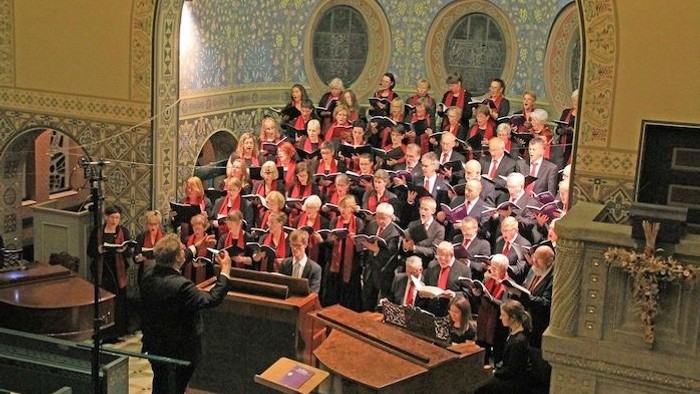 Ein großer Chor singt in einer prächtigen Kirche, dirigiert von einem Mann am Klavier