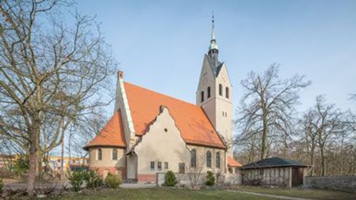Kleine Kirche mit hohem Turm und rotem Dach in ländlicher Umgebung