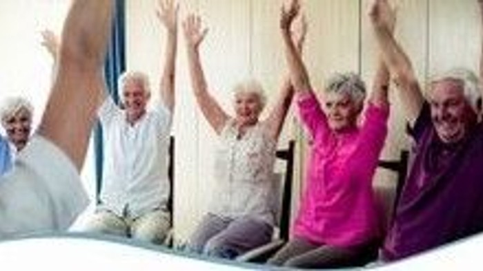 Senioren sitzen im Kreis auf Stühlen und strecken alle die Arme und Hände in die Luft.