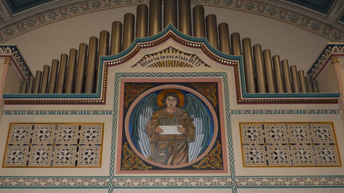 Das Bild zeigt eine verzierte Kirchenorgel mit einem religiösen Gemälde in der Mitte.