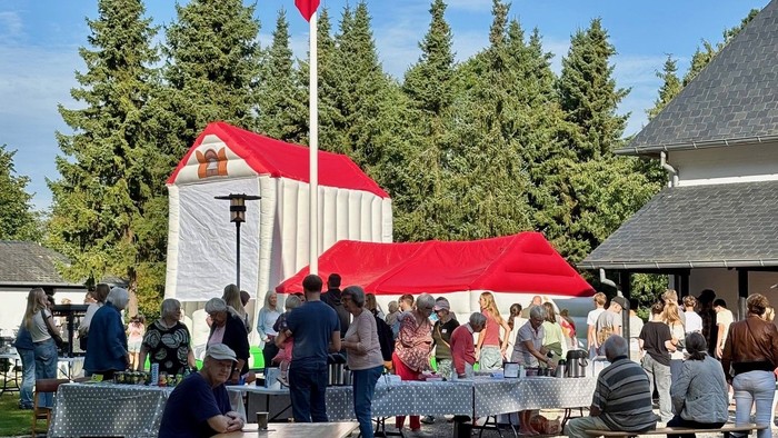 Udendørs samvær med et norsk flag, røde telte og folk, der hygger sig under klar himmel.