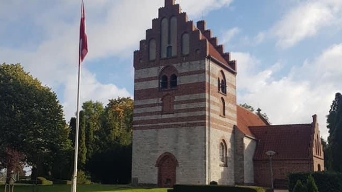 En kvinde går forbi en historisk bygning med tårn og flagstang.