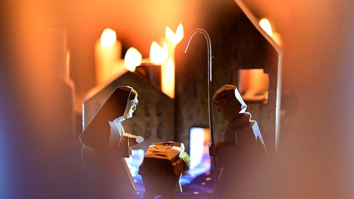 Maria und Josef aus Holz mit Kerzen, im Hintergrund angedeutet ein paar Häuser