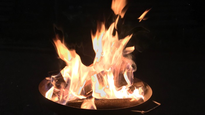 Lebhaftes Feuer, das hell in einer Metall-Feuerstelle brennt, umgeben von einem nächtlichen Wald.