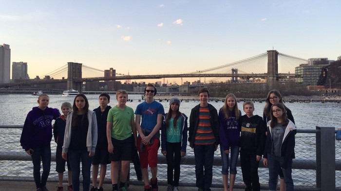 En gruppe unge står sammen ved vandet med Brooklyn Bridge i baggrunden