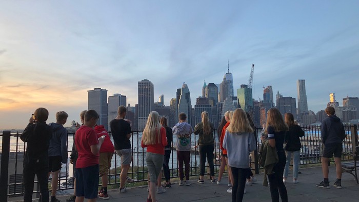 En gruppe mennesker ser på New York Citys skyline ved solnedgang.