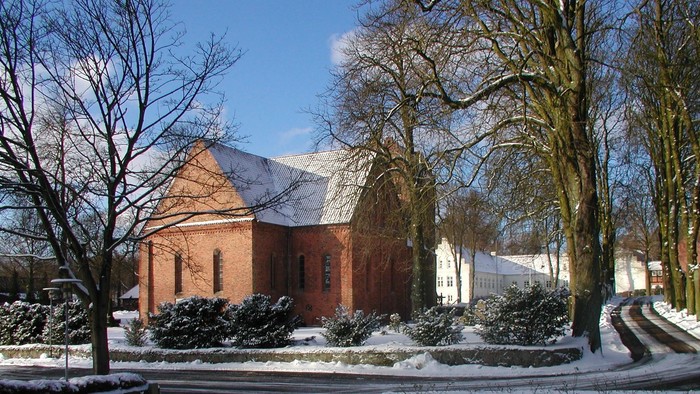 En rød murstenskirke med tagtag i snefaldende landskab