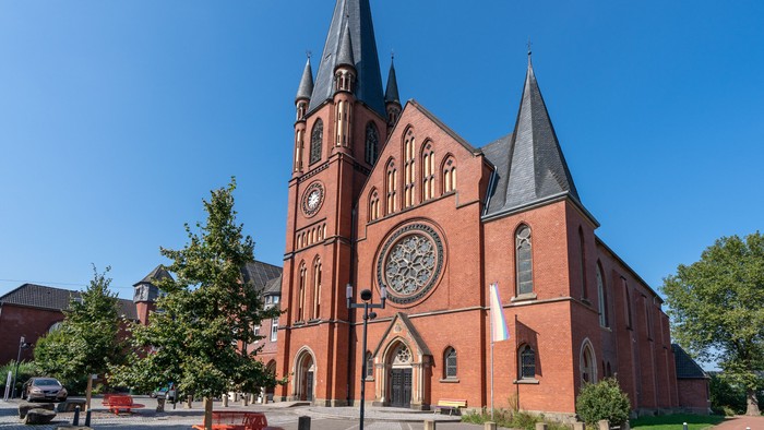 Auffällige Backsteinkathedrale mit Zwillingstürmen und einer markanten Uhr unter einem klaren blauen Himmel.