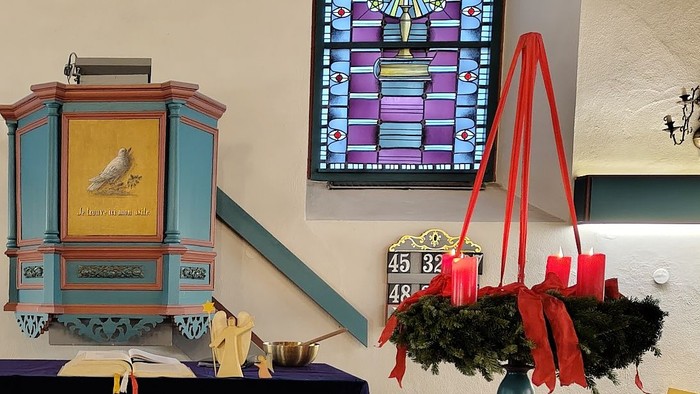 Verzierte Weihnachtskrippe mit Weihnachtsbaum, Kirchenfenstern aus Buntglas und festlichen Altarverzierungen in einer Kapelle.