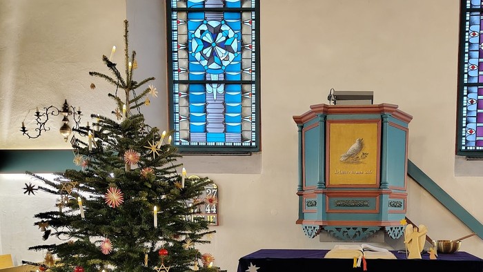 Verzierte Weihnachtskrippe mit Weihnachtsbaum, Kirchenfenstern aus Buntglas und festlichen Altarverzierungen in einer Kapelle.