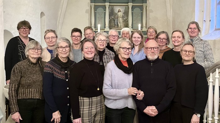 Gruppe af mennesker, der poser sammen indendørs i en kirke med religiøs kunst i baggrunden.