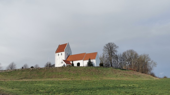 En hvid kirke med røde tag på en bakke med græs.