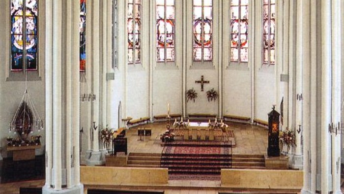 Innenraum einer Kirche mit hohen Säulen und buntem Glasfenster