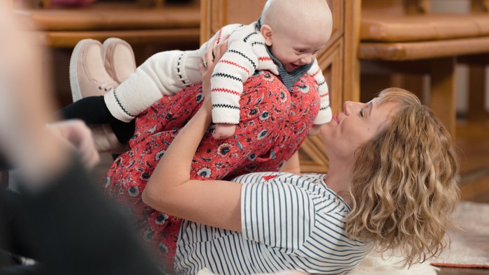 En kvinde løfter legende en baby i en hyggelig indendørs omgivelse mens hun smiler.