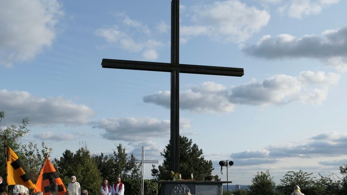 Eine große Menschenmenge versammelt sich vor einem hohen Kreuz unter einem bewölkten Himmel.